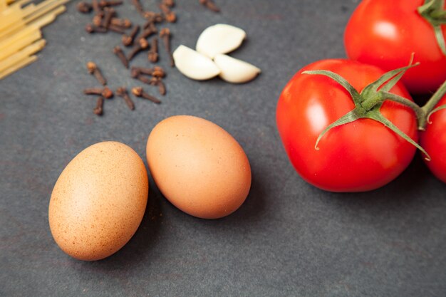 Pasta ingredients. Tomatoes, spaghetti pasta, garlic, eggs and spices on dark grunge backdrop, close up. horizotal oriented