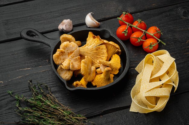 Pasta ingredients with raw mushrooms chanterelles set, on black wooden table background