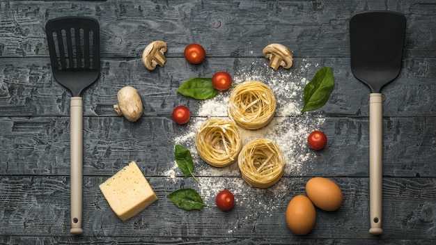 Pasta, kaas, champignons en tomaten met keukenspatels op een houten ondergrond. Ingrediënten voor het maken van pasta.