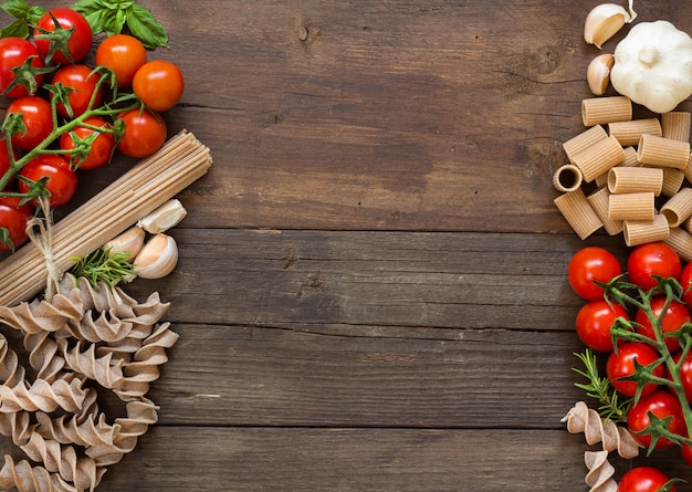 Pasta, knoflook, kruiden en tomaten op bruin houten tafelblad bekijken met kopie ruimte