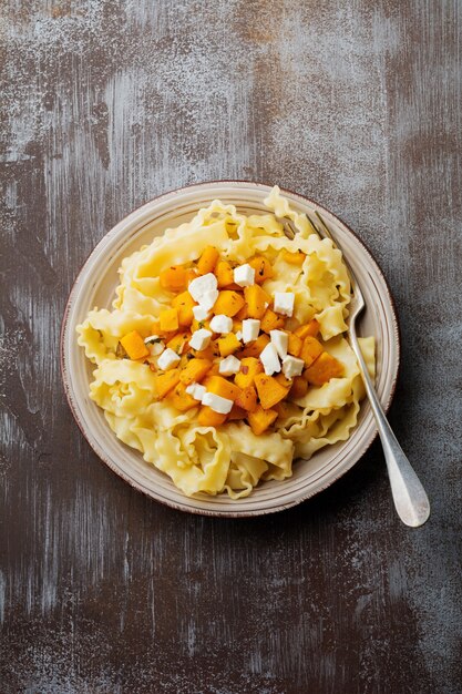 Pasta Mafaldine Napoletane with baked pumpkin, feta cheese and seasoning herbs in ceramic plate. Rustic style. Top view.