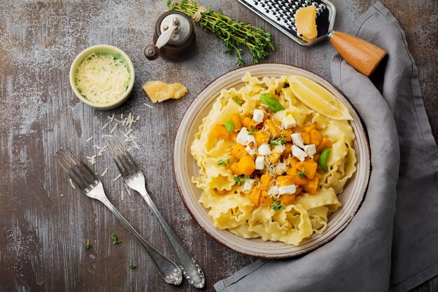 Pasta Mafaldine Napoletane with baked pumpkin, feta cheese and seasoning herbs in ceramic plate. Rustic style. Top view.