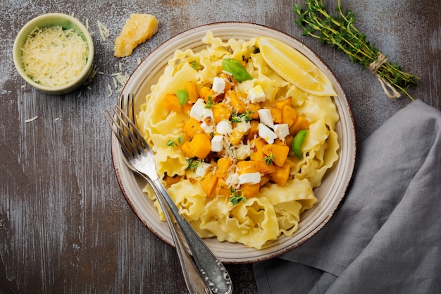 Pasta Mafaldine Napoletane with baked pumpkin, feta cheese and seasoning herbs in ceramic plate. Rustic style. Top view.