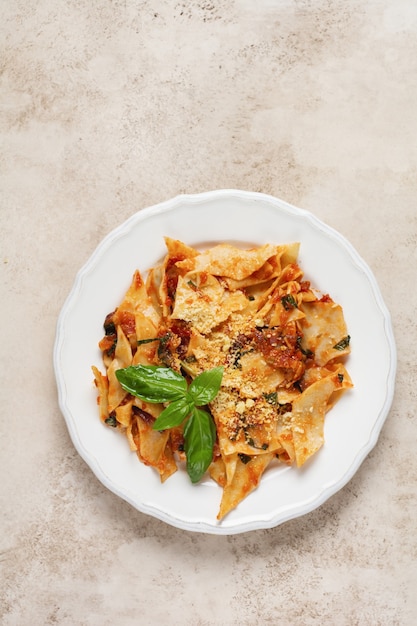 Pasta Maltagliati with classic tomato sauce, parmesan and basil on a rustic concrete light table. Traditional Italian dish serving. Top view.