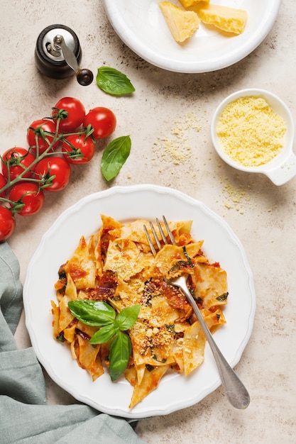 素朴なコンクリートのライトテーブルにクラシックなトマトソース、パルメザンチーズ、バジルを添えたマルタリアーティパスタ。伝統的なイタリア料理を提供しています。上面図。