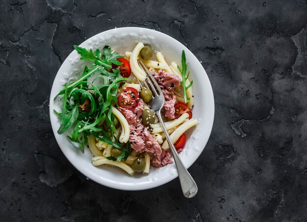 Pasta met ingeblikte tonijn, olijven en kerstomaatjes op een donkere achtergrond bovenaanzicht