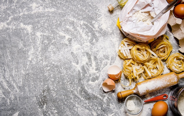 Pasta met ingrediënten - bloem, eieren en verschillende gereedschappen om te koken. Op de stenen tafel. Vrije ruimte voor tekst. Bovenaanzicht