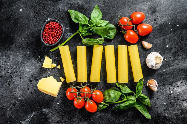 Pasta met rauwe cannelloni. italiaanse keuken. kookingrediënten: basilicum, kerstomaatjes, parmezaan, knoflook. zwarte achtergrond. bovenaanzicht