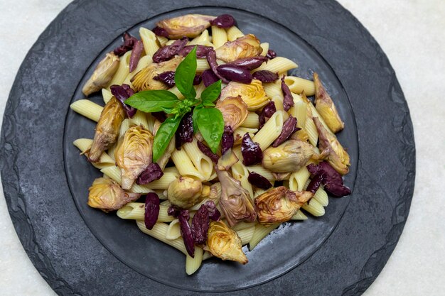 Pasta met zwarte olijven en artisjokharten, gegarneerd met verse basilicumblaadjes.