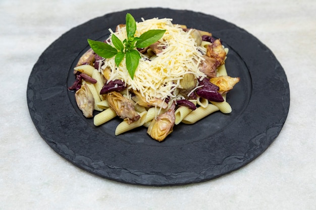 Pasta met zwarte olijven, Parmezaanse kaas, artisjokharten, gegarneerd met verse basilicumblaadjes.