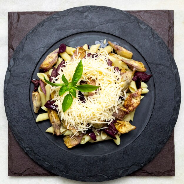 Pasta met zwarte olijven, Parmezaanse kaas, artisjokharten, overgoten met verse basilicumblaadjes.