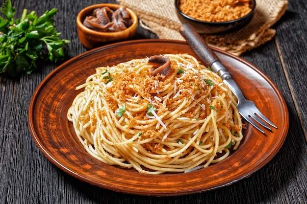 Pasta mollicata: spaghetti met ansjovis en geroosterde broodkruimels, Parmezaanse kaas en peterselie - traditionele Zuid-Italiaanse schotel, geserveerd op een bord op een donkere houten achtergrond, bovenaanzicht, close-up