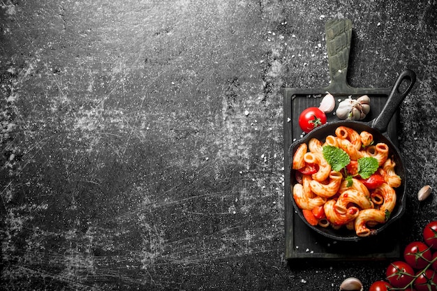 Pasta in pan on a cutting Board with garlictomato and mint leaves