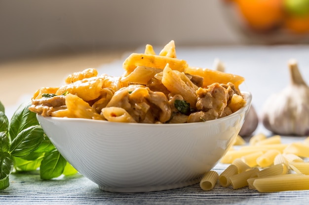 Pasta penne with chicken pieces mushrooms basil and parmesan cheese  Italian food in white bowl on kitchen table.