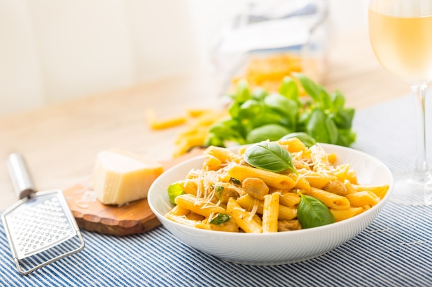 Pasta penne with chicken pieces mushrooms basil parmesan cheese and white wine.  Italian food in white plate on kitchen table.