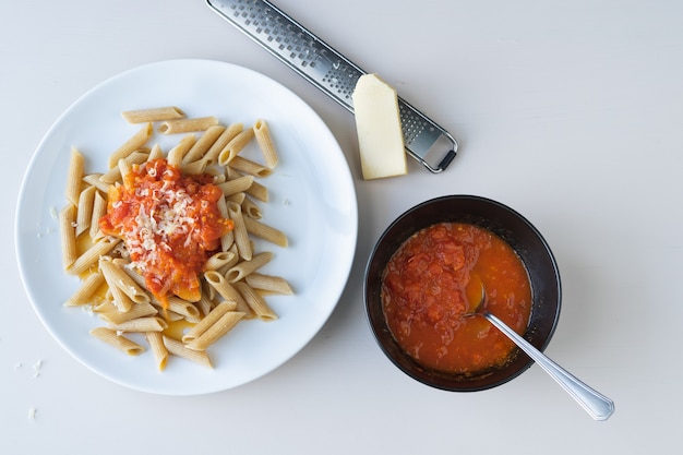 Piatto di pasta con pomodoro su sfondo bianco. pezzo di formaggio e grattugia. ciotola con pomodoro. copia spazio. vista dall'alto.