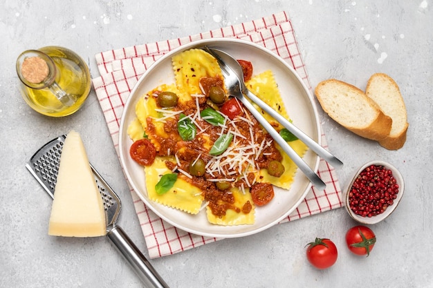 Foto ravioli di pasta con salsa di pomodoro e olive con basilico e formaggio su fondo grigio