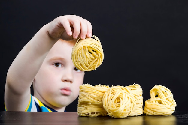 Pasta in raw dried form in the hands of a little boy, real noodles and pasta, closeup in the kitchen