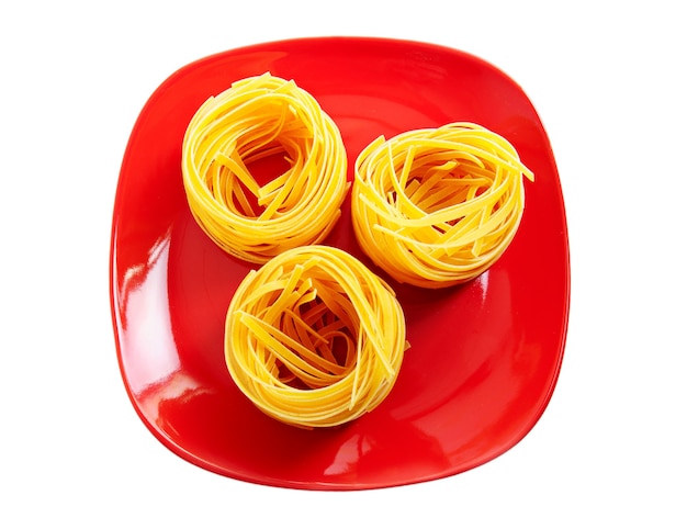 Pasta raw nests on red dish isolated