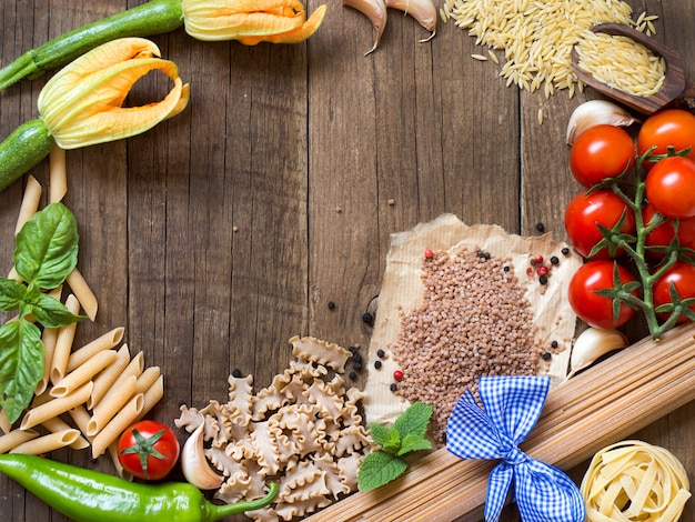 Pasta and raw vegetables on wooden background top view with copy space