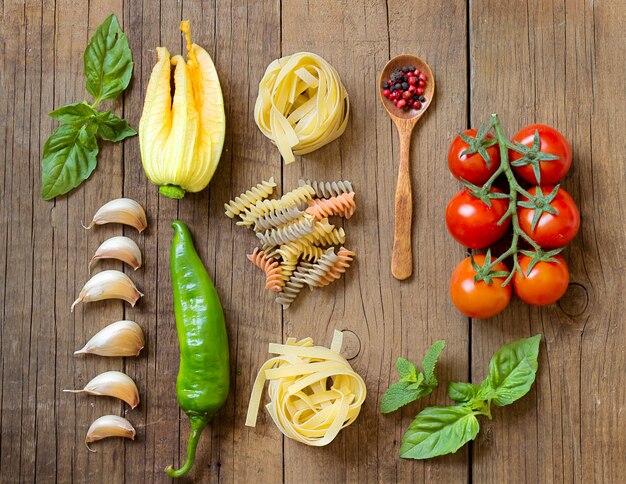 Pasta and raw vegetables on wooden background top view with copy space