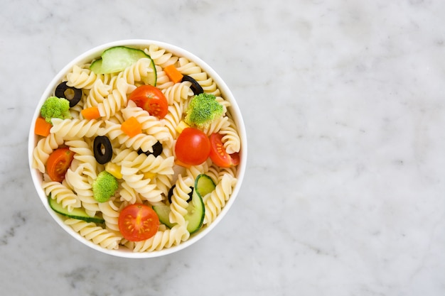 Pasta salad in a bowl on white marble top view 