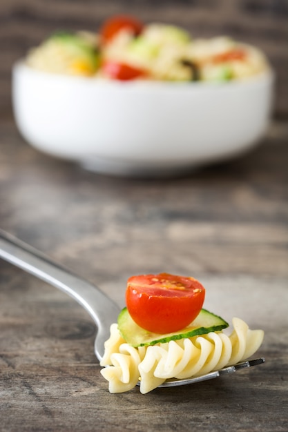 Pasta salad on fork with vegetables on rustic wooden table