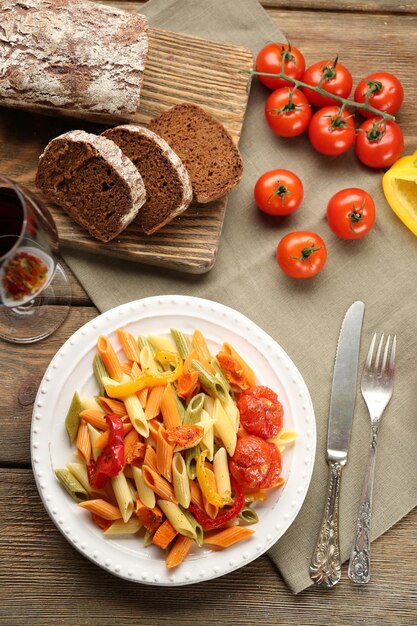 Pasta salad with pepper carrot and tomatoes on wooden table background