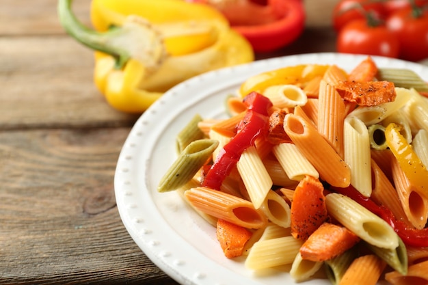 Pasta salad with pepper carrot and tomatoes on wooden table background