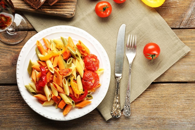 Pasta salad with pepper carrot and tomatoes on wooden table background