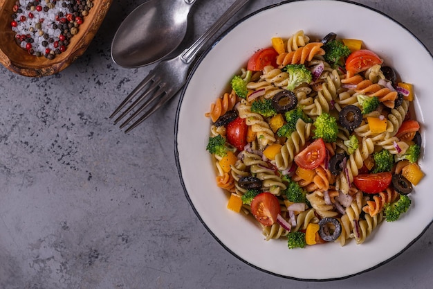 Pasta salad with tomato, broccoli, black olives. Top view