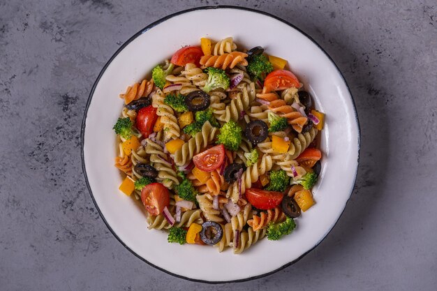 Pasta salad with tomato, broccoli, black olives. Top view