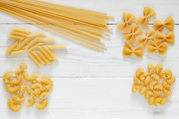 Pasta set of raw farfalle spaghetti pipe maccheroni penne cresta on white wooden board background top view space to copy text