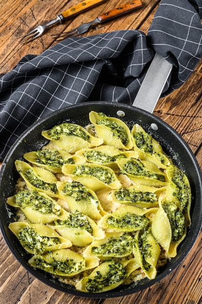 Pasta shells Conchiglioni stuffed with spinach and cheese baked with sauce in a pan. Wooden background. Top view.