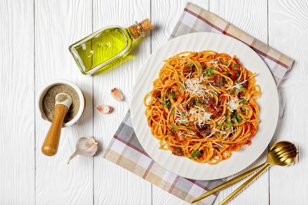 Pasta spaghetti alla norma op een witte plaat op een witte getextureerde houten tafel met ingrediënten, italiaanse keuken, horizontale weergave van bovenaf, plat gelegd