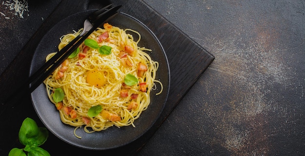 Pasta spaghetti carbonara met spek, Parmezaanse kaas, eigeel en basilicum bladeren op zwarte achtergrond. Traditioneel Italiaans gerecht. Bovenaanzicht.