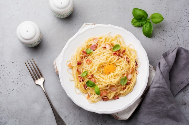 Pasta spaghetti carbonara with bacon, parmesan cheese, egg yolk and basil leaves on gray light surface. Traditional Italian dish