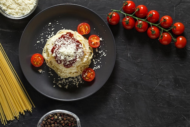 Pasta spaghetti italiaans met parmezaanse kaas en ingrediënten om te koken, tomaten, kruiden, macaroni, geraspte kaas, bovenaanzicht donkere achtergrond, met ruimte om tekst te kopiëren.