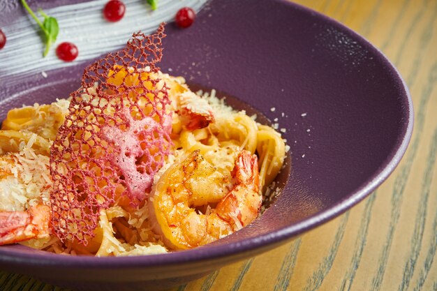 Pasta spaghetti met garnalen en Parmezaanse kaas. Pasta met zeevruchten in een paarse kom tegen een houten oppervlak. Italiaanse keuken