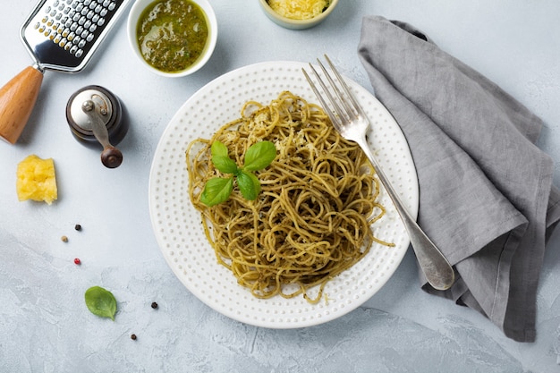 Pasta spaghetti met pestosaus, basilicum en parmezaanse kaas op een witte keramische plaat en een grijze betonnen ondergrond