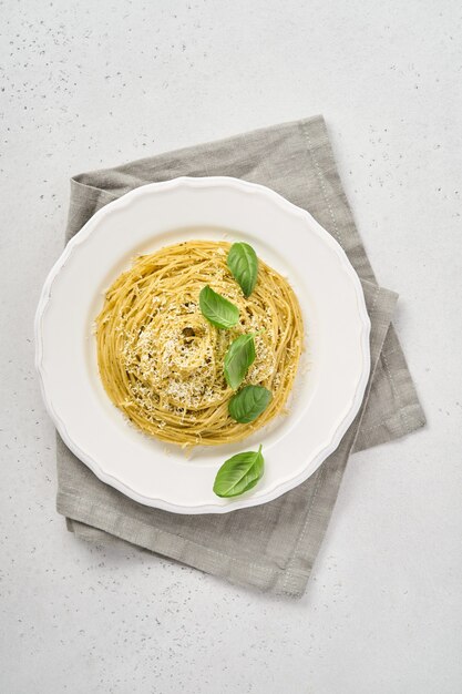 Pasta spaghetti met pestosaus en verse basilicum bladeren in witte kom.