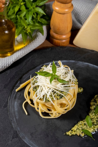 Pasta spaghetti met pestosaus en verse basilicum bladeren in zwarte stenen schotel op houten achtergrond.