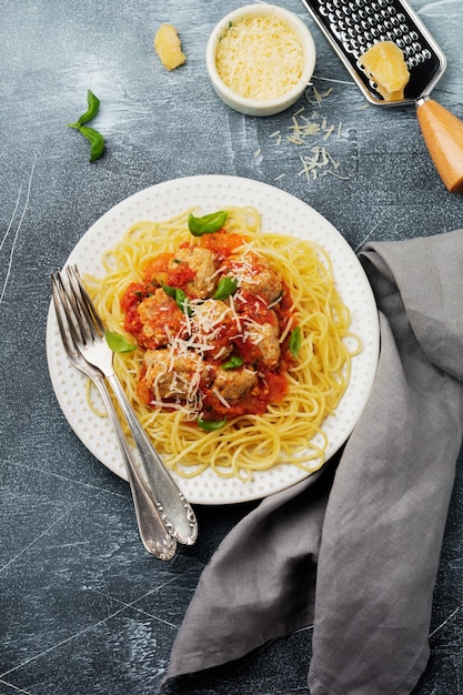 Pasta spaghetti met tomatensaus, Parmezaanse kaas, basilicum en gehaktballen op witte keramische plaat op grijs beton