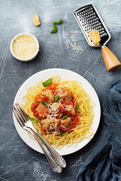 Pasta spaghetti met tomatensaus, parmezaanse kaas, basilicum en gehaktballen op witte keramische plaat op grijze betonnen ondergrond