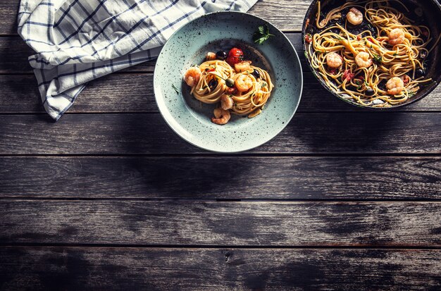 Паста спагетти на тарелке и сковороде с помидорами, соусом из креветок и зеленью. Итальянская или средиземноморская кухня.
