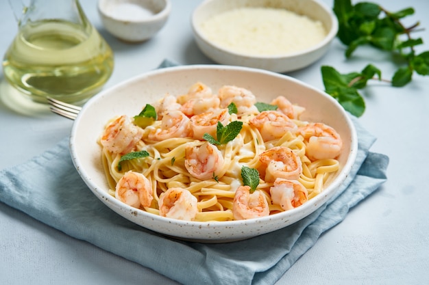 Pasta spaghetti with grilled shrimps, bechamel sauce, mint leaf on blue table, italian cuisine