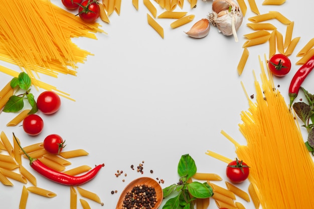 Spaghetti della pasta con gli ingredienti per la cottura della pasta su un fondo bianco, vista superiore.