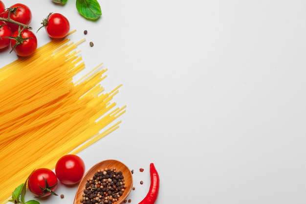 Spaghetti della pasta con gli ingredienti per la cottura della pasta su un fondo bianco, vista superiore.