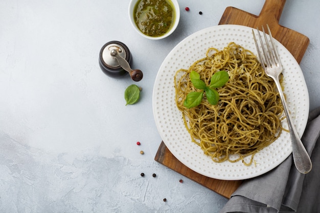 Pasta spaghetti with pesto sauce, basil and parmesan cheese on a white ceramic plate and gray concrete or stone surface. Traditional Italian dish. Selective focus. Top view.