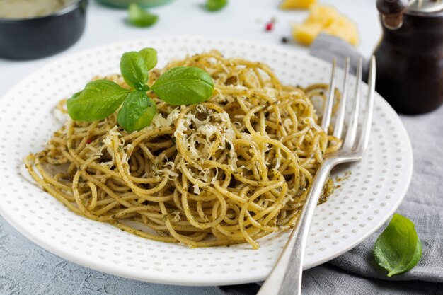 Pasta spaghetti with pesto sauce, basil and parmesan cheese on a white ceramic plate and gray concrete surface